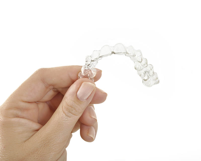 Woman displaying a clear aligner by invisalign in her hand